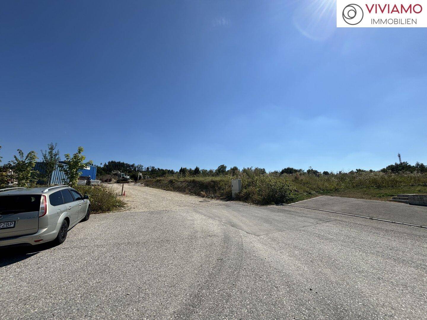 Gepflasterter Zufahrtsbereich mit einem geparkten Fahrzeug und weitem Blick auf die grüne Umgebung unter blauem Himmel.