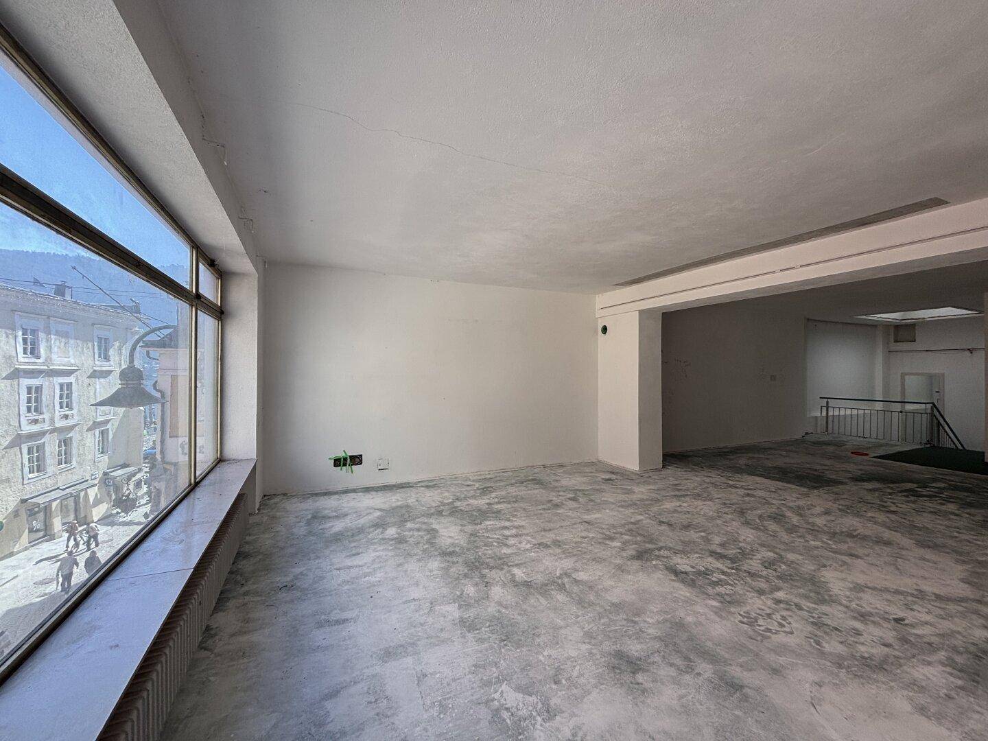 Geräumiger, unmöblierter Raum mit großen Fenstern und Blick auf die Straße, bereit für den Ausbau.