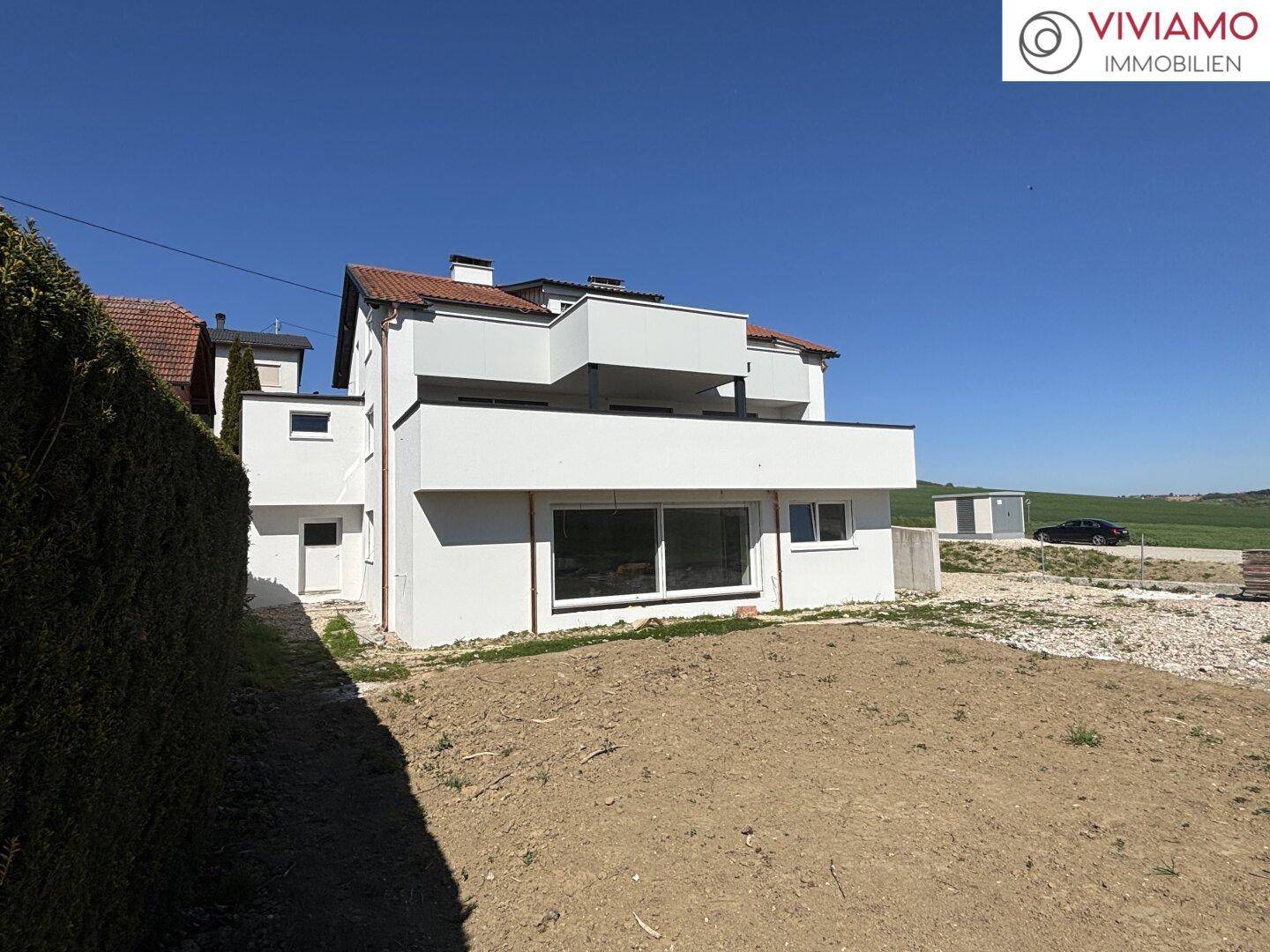 Moderne Doppelhaushälfte mit Balkonen und ungestaltetem Gartenbereich.