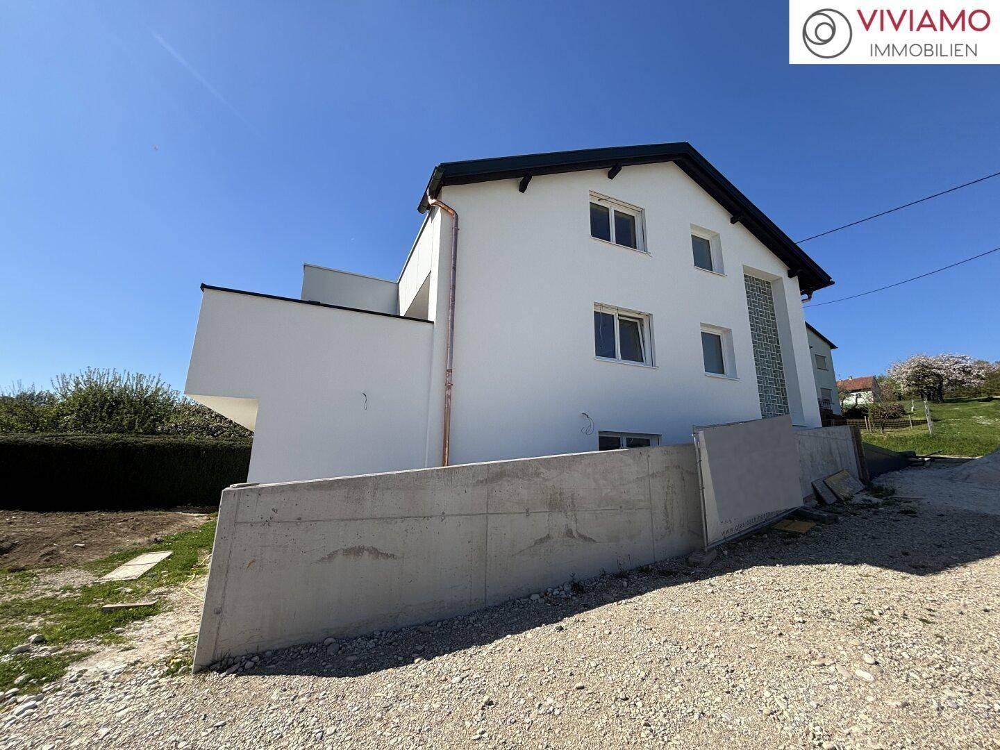 Seitenansicht der modernen Doppelhaushälfte mit weißer Fassade und Betonmauer.