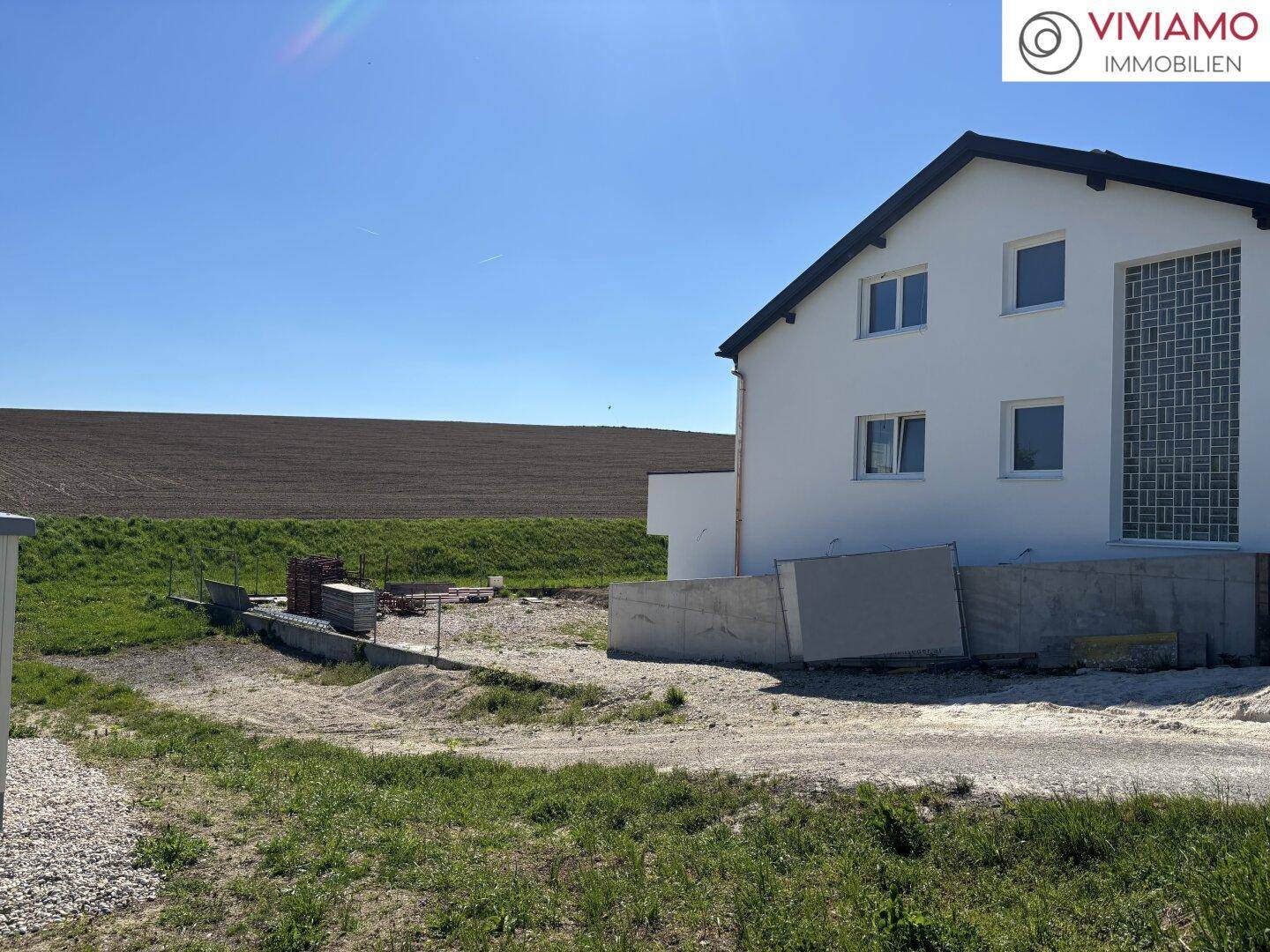 Seitenansicht der Doppelhaushälfte mit weißer Fassade und angrenzendem Baugelände.