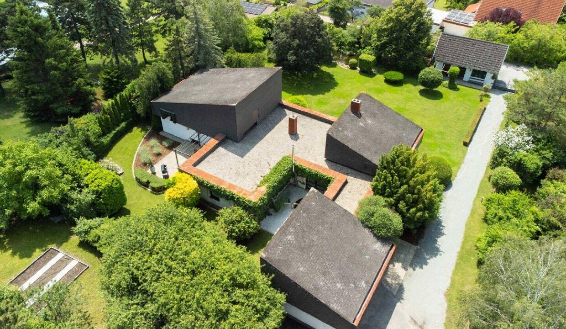 Luftaufnahme des Hauses mit Flachdach und gepflegtem Garten, umgeben von viel Grün.