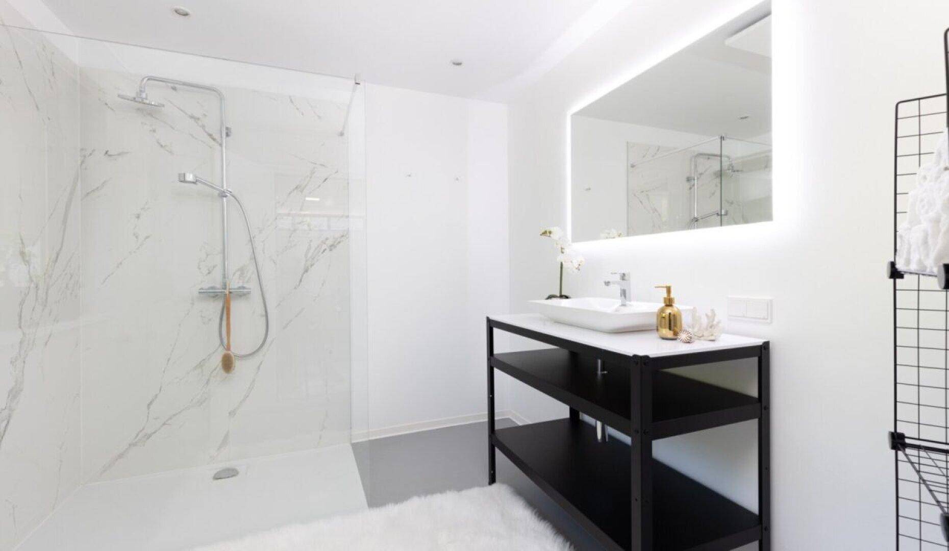 Modernes Badezimmer mit großer begehbarer Dusche, eleganten Marmorfliesen und beleuchtetem Spiegel.