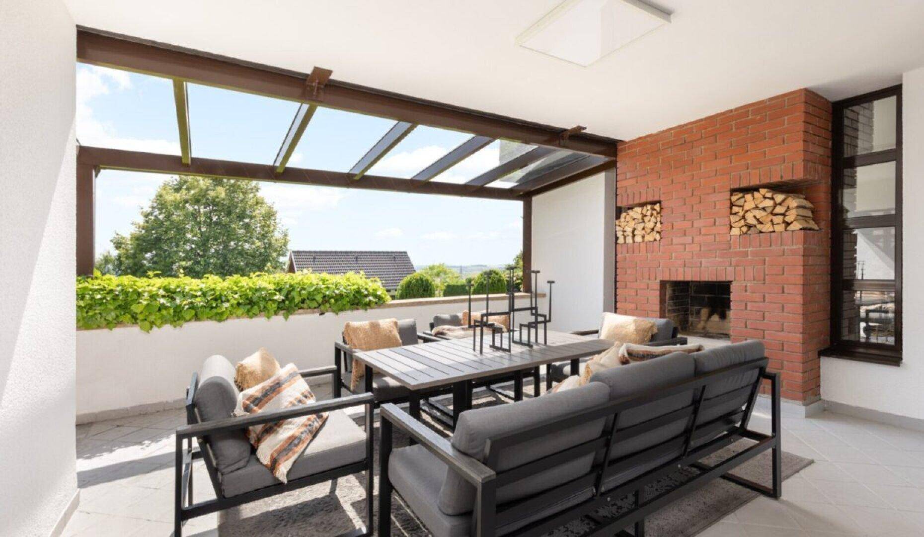 Überdachte Terrasse mit Außenkamin, bequemen Loungemöbeln und weitem Blick ins Grüne.