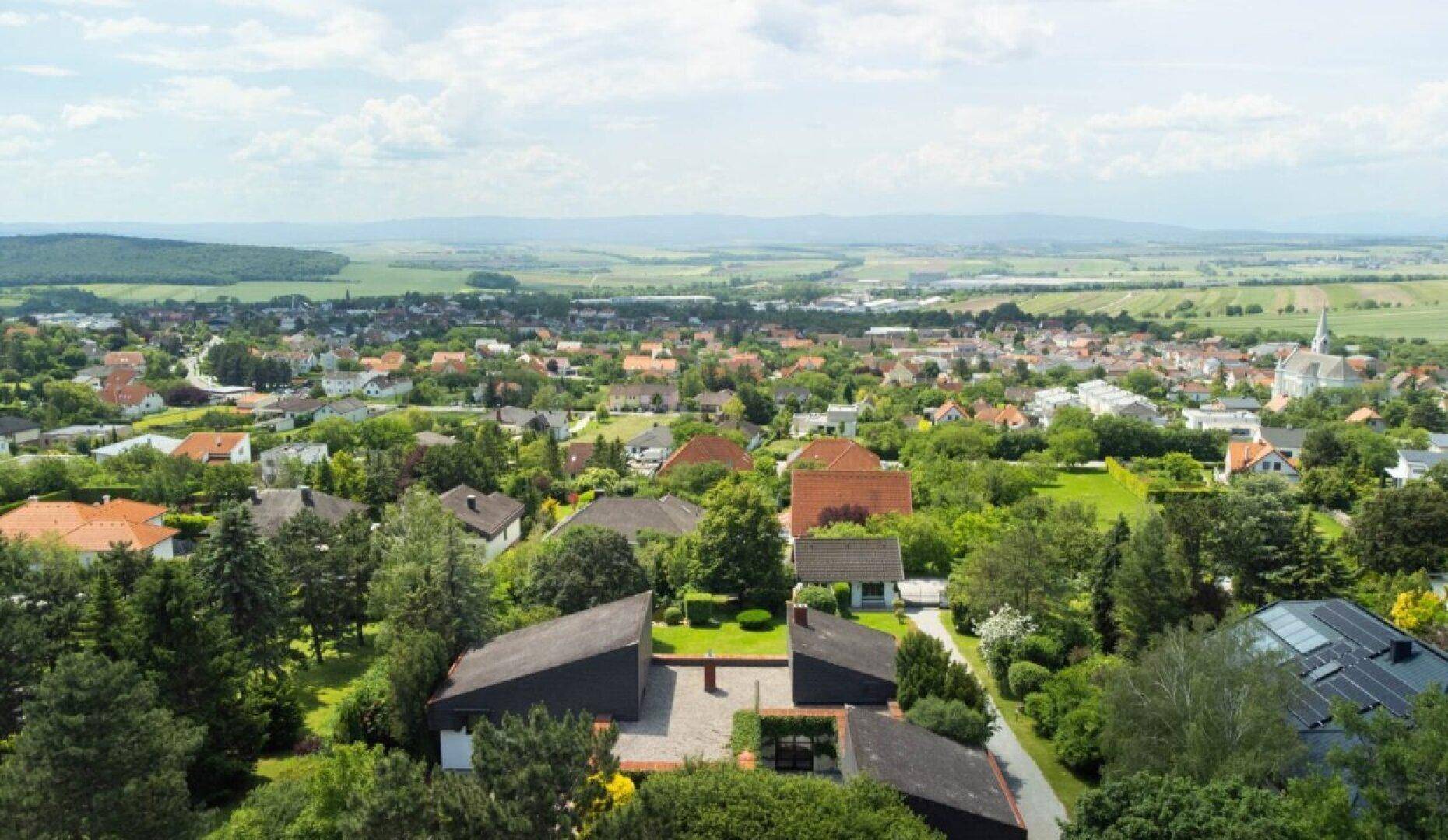 Weitläufige Luftaufnahme der Siedlung mit dem Anwesen im Vordergrund und hügeliger Landschaft.