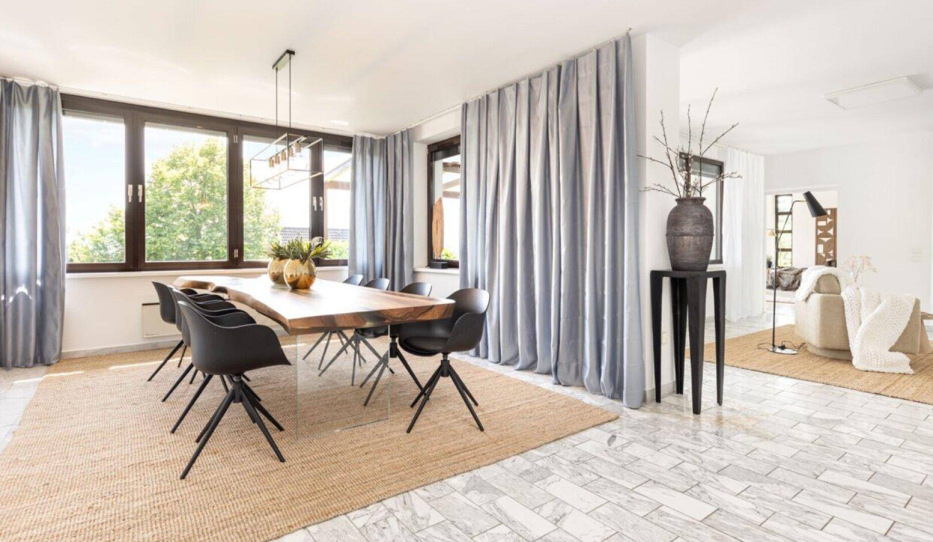 Eleganter Essbereich mit großem Holztisch, modernen Stühlen und hellen Vorhängen, viel Tageslicht.