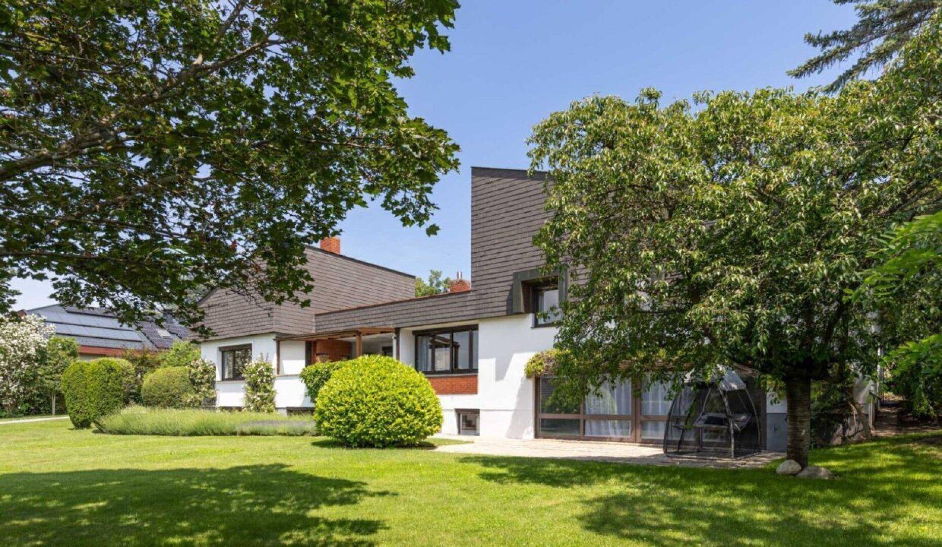 Weitläufiger Garten mit Rasenfläche, Bäumen und Blick auf die moderne Hausfassade.