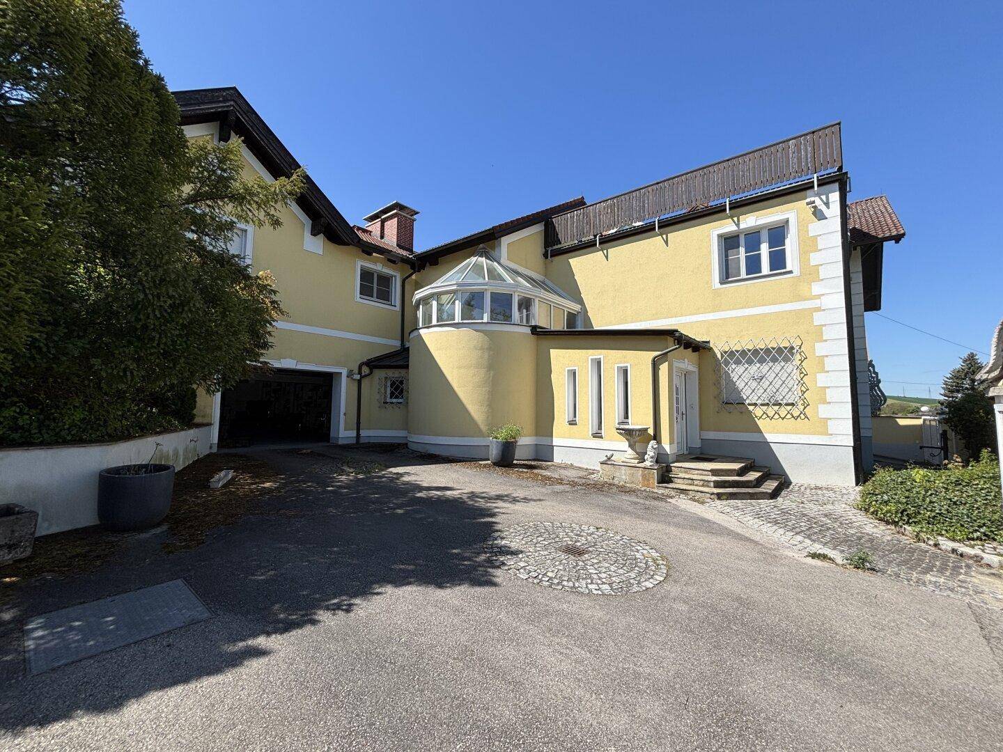 Eingangsbereich der Villa mit gepflasterter Auffahrt und einem Wintergarten-Anbau.