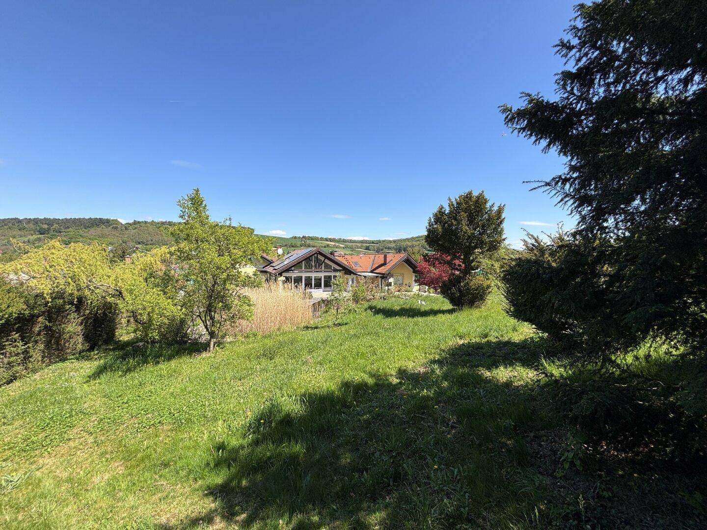 Weitläufiger Blick über das Anwesen und die grüne Hügellandschaft unter blauem Himmel.