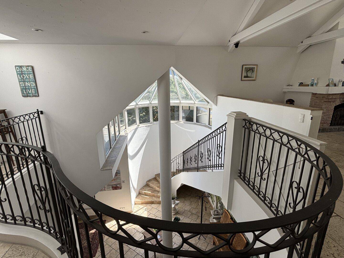 Elegante Wendeltreppe mit schmiedeeisernem Geländer und einem lichtdurchfluteten Glasdach.
