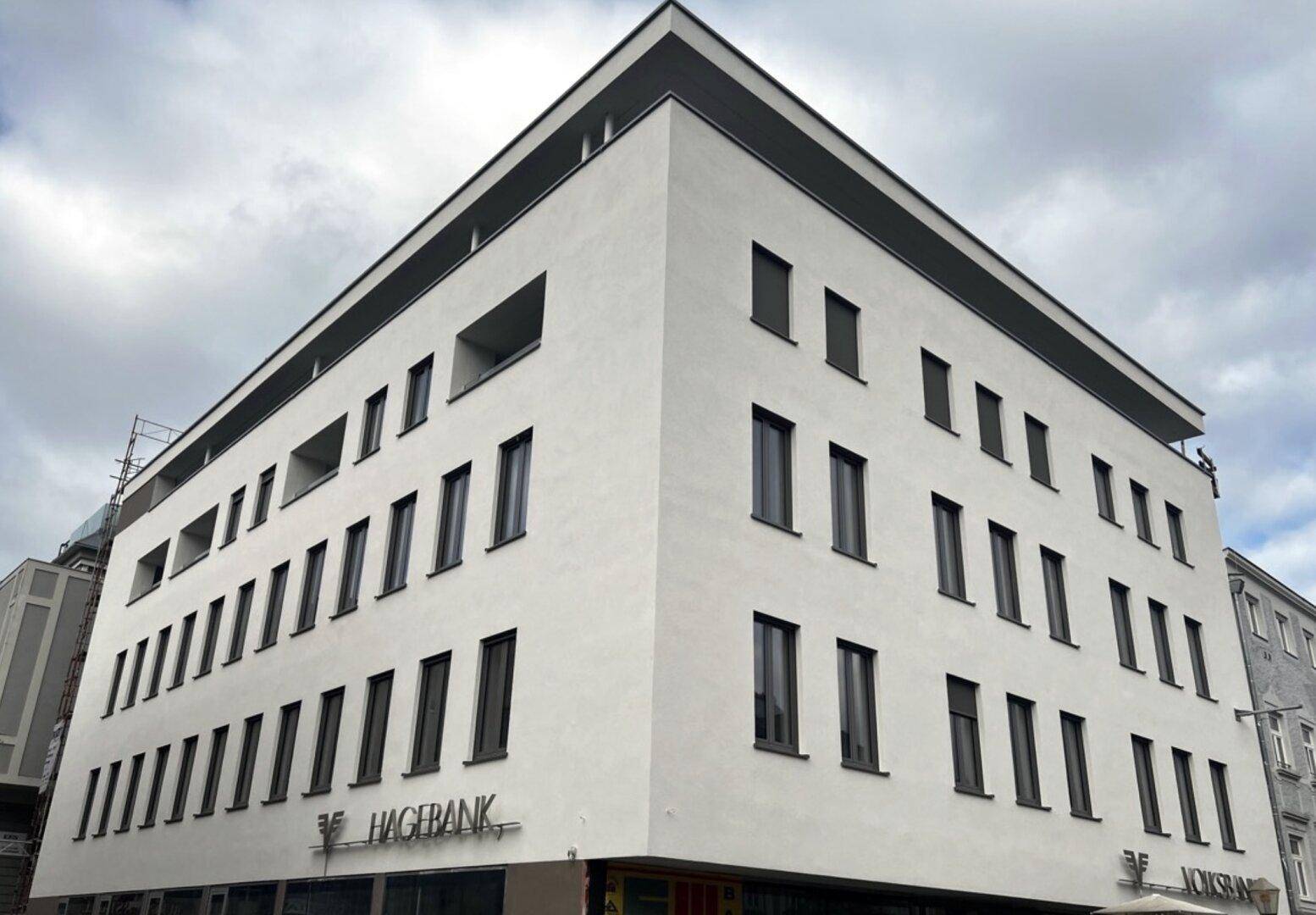 Moderne Gebäudefassade mit weißem Putz, vielen Fenstern und einem Banklogo im Erdgeschoss.