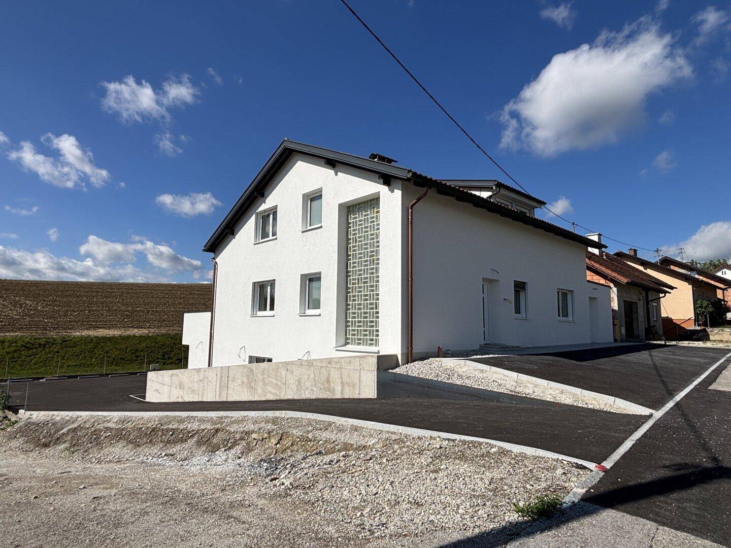 Seitenansicht des Neubaus mit weißer Fassade, dekorativem Element und neu angelegter Zufahrt.
