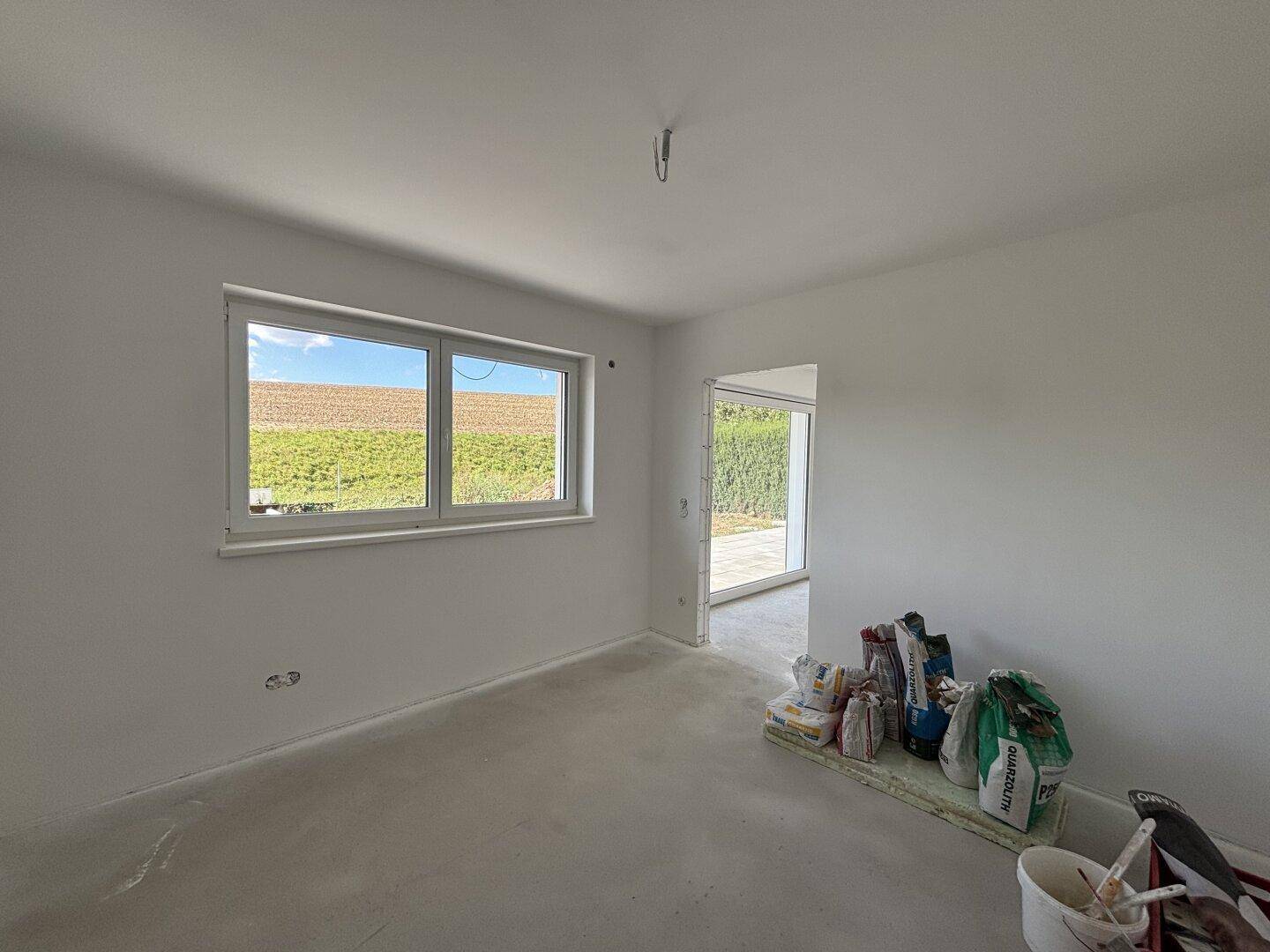 Helles Zimmer im Rohbau mit Fenster und weitem Blick über die Felder.