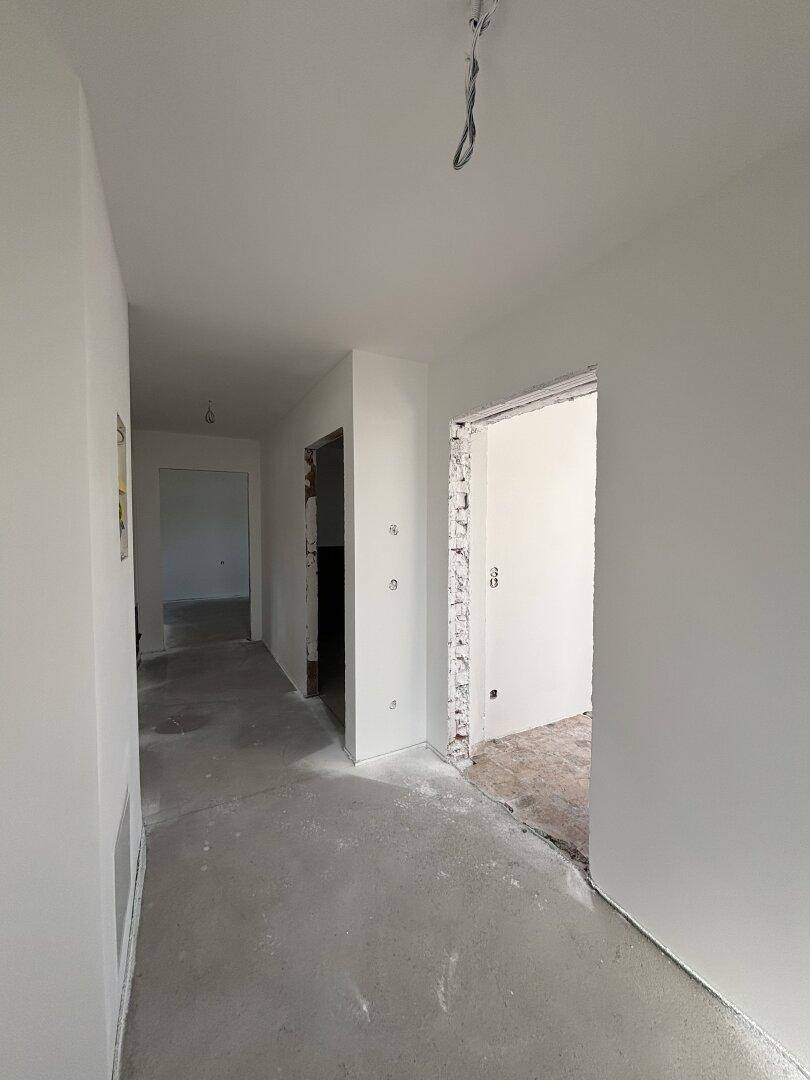Unfertiger Flur mit weißen Wänden und Rohbetonboden, bereit für den weiteren Ausbau.