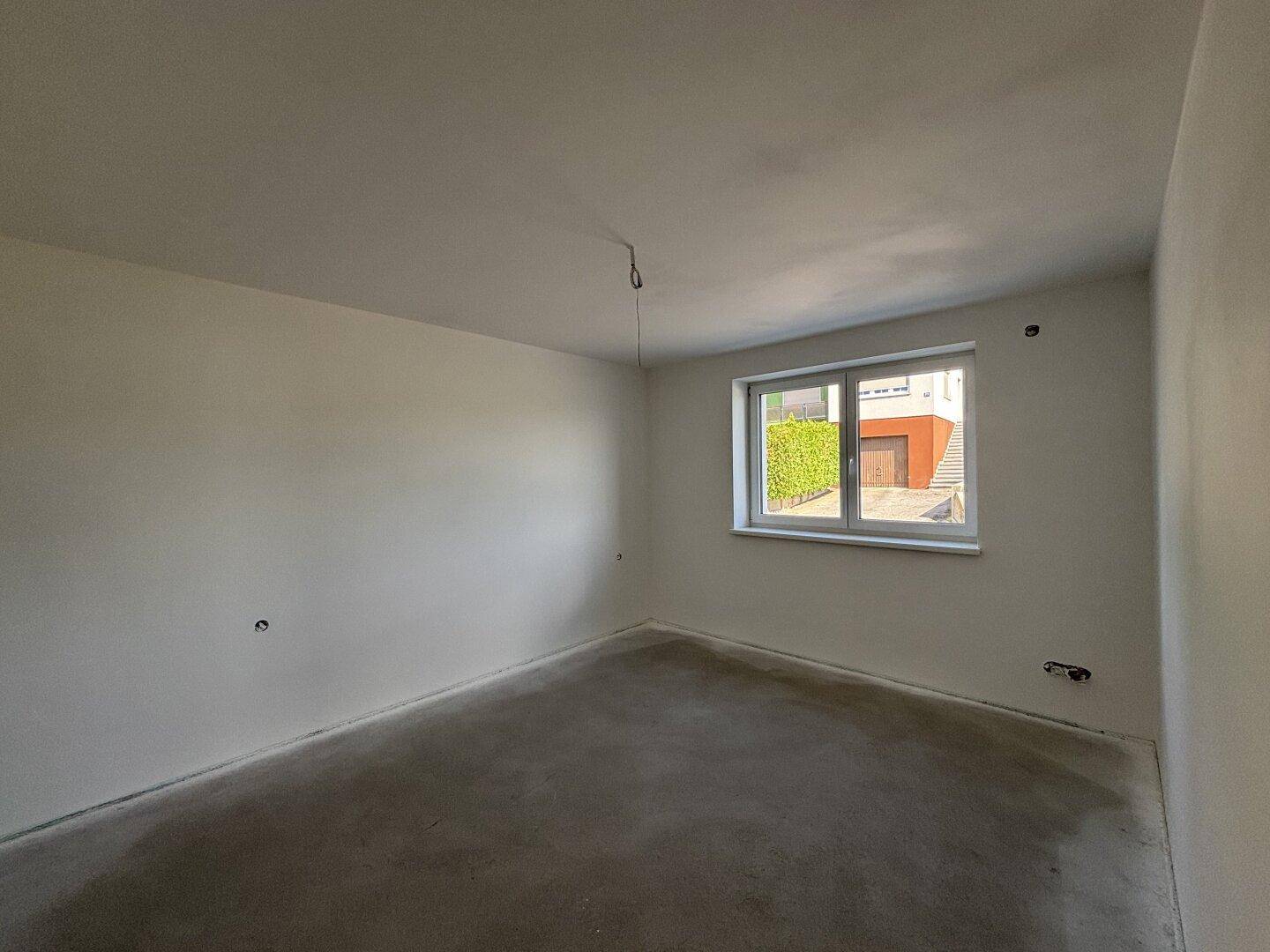 Unfertiges Schlafzimmer mit weißen Wänden und Rohbetonboden, bereit für die individuelle Gestaltung.