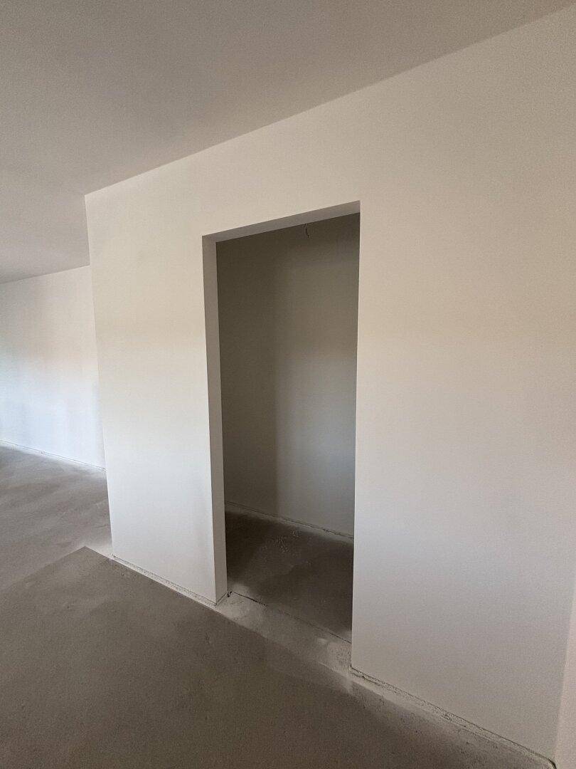 Leerer Abstellraum oder Nische mit weißen Wänden und Rohbetonboden, bereit für die Nutzung.