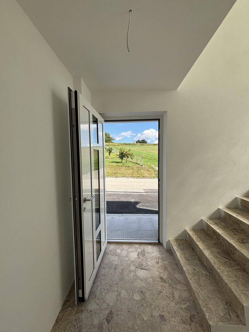 Heller Eingangsbereich mit Marmorfliesenboden und Treppe, mit Blick ins Grüne durch die offene Tür.
