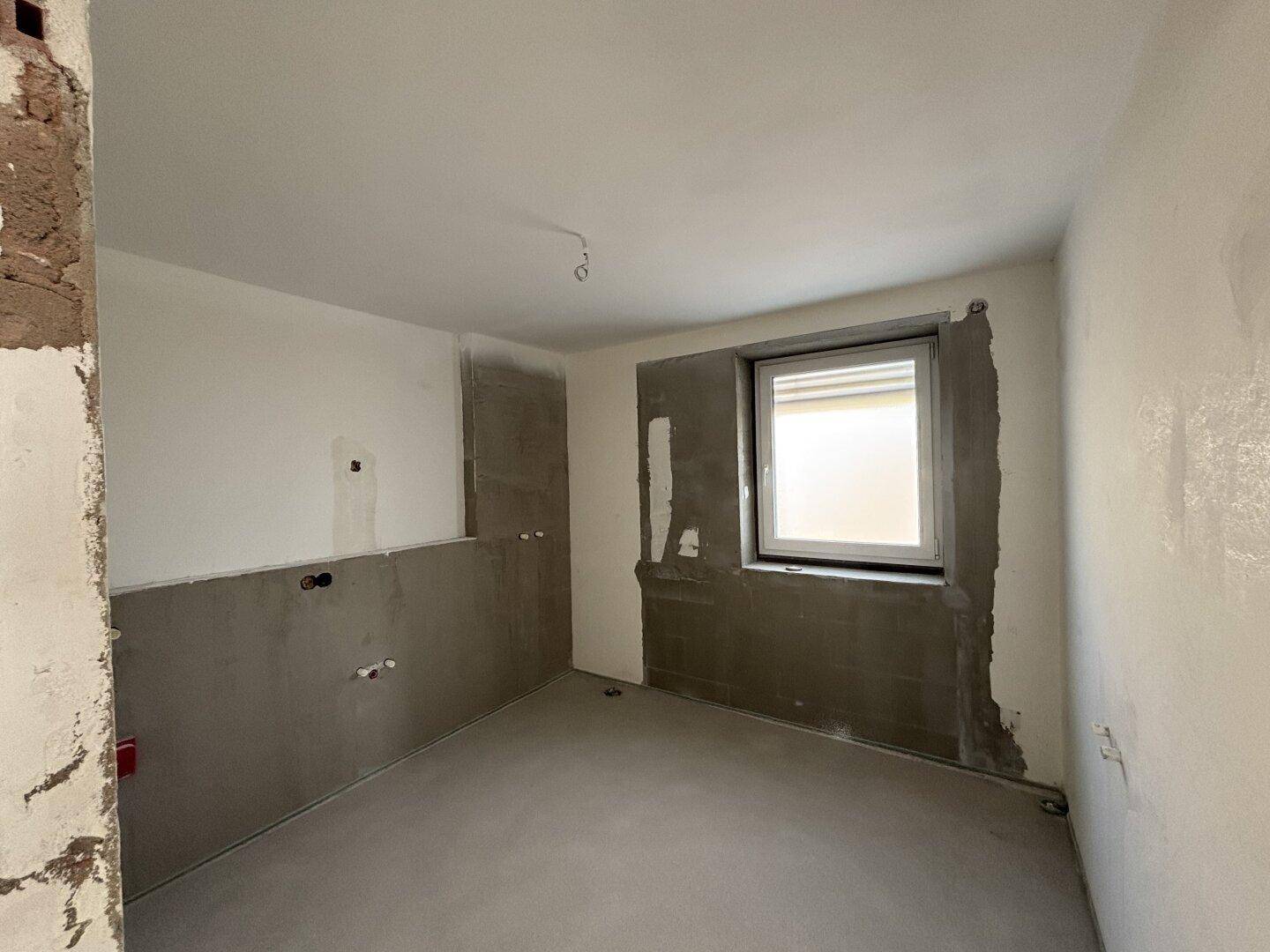 Unfertiger Raum, möglicherweise ein Badezimmer oder Hauswirtschaftsraum, mit Fenster und vorbereiteten Wänden.