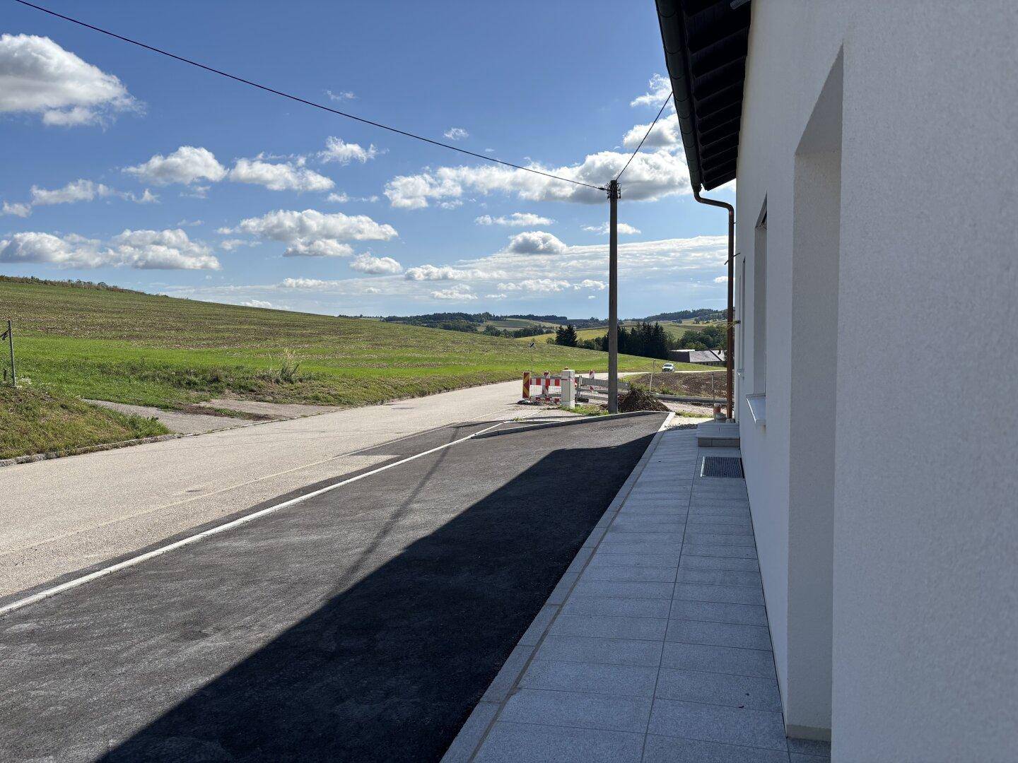 Ruhige Landstraße neben dem Grundstück mit weitem Blick über grüne Hügel und Felder.