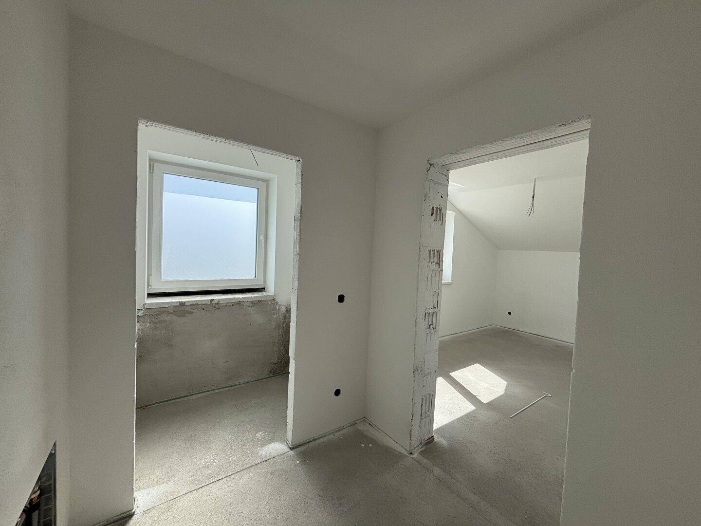 Zwei unfertige Räume im Dachgeschoss mit Rohbauwänden und einem Fenster mit Milchglas.