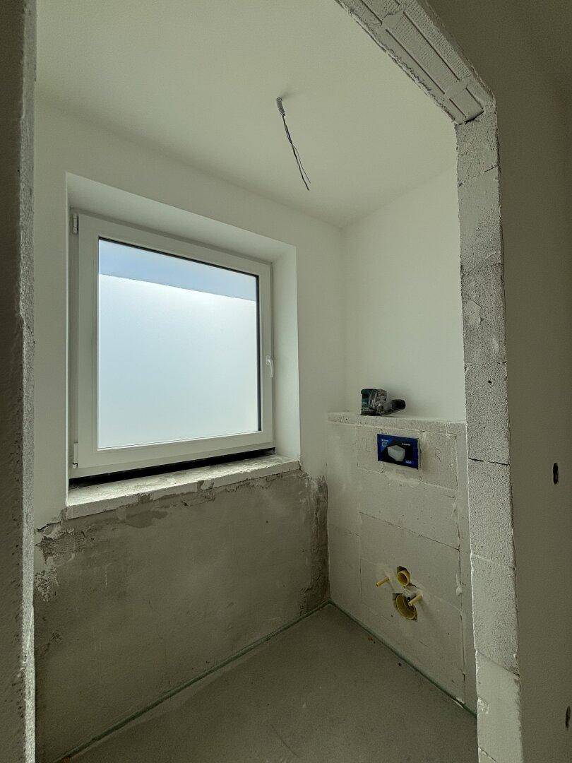Unfertiges Badezimmer oder WC mit Fenster und Vorinstallationen für Sanitäranlagen.