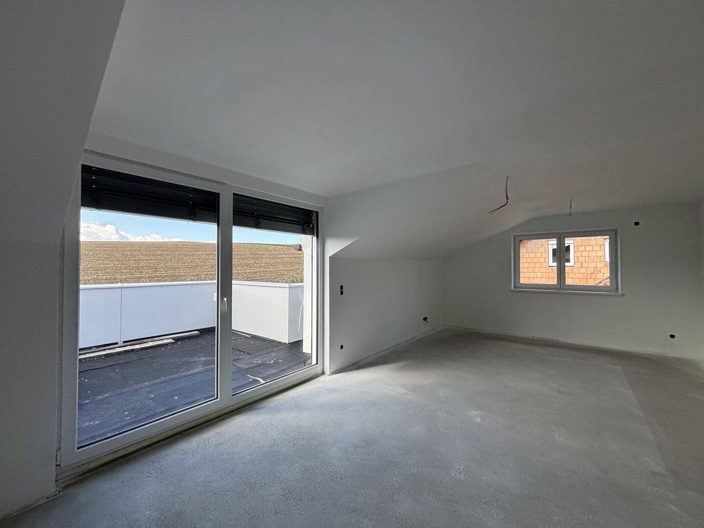 Großer, heller Raum im Dachgeschoss mit Zugang zur Dachterrasse und Dachschrägen.