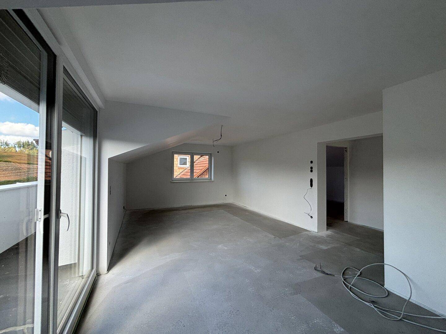 Geräumiger, unfertiger Raum im Dachgeschoss mit Zugang zu einer Terrasse und Dachschrägen.