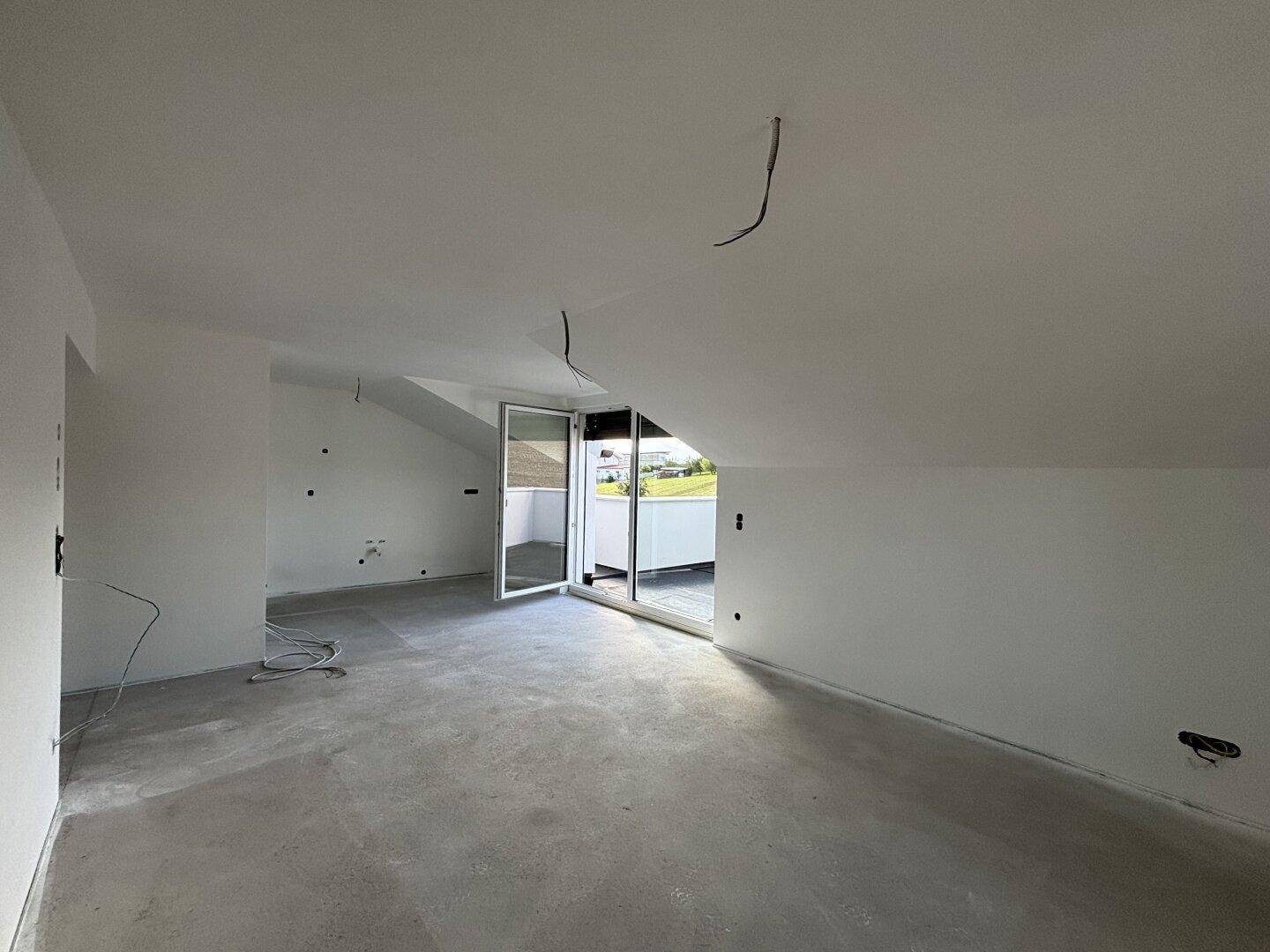 Geräumiger, unfertiger Raum im Dachgeschoss mit Zugang zur Dachterrasse und Dachschrägen.