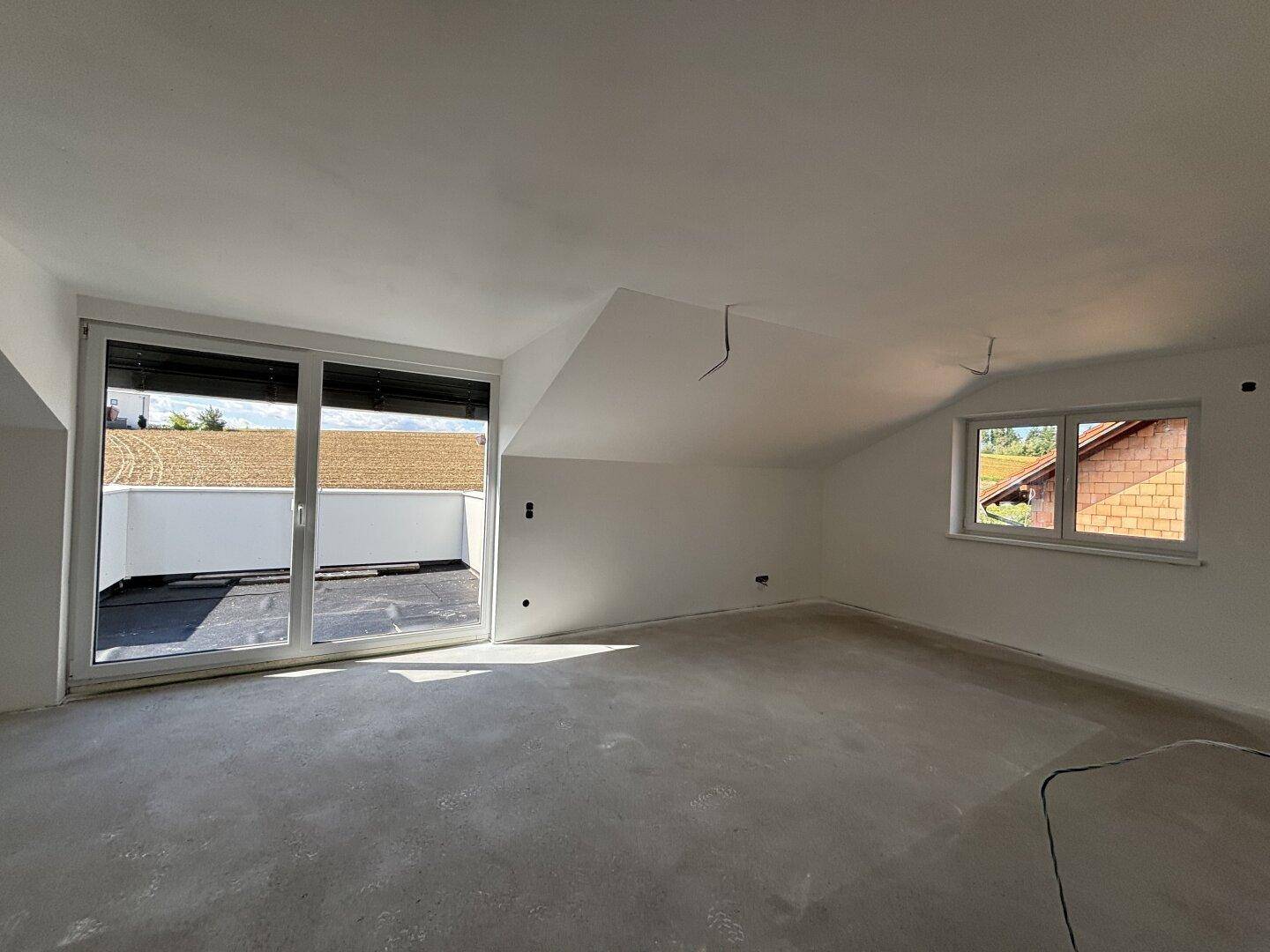 Heller, unfertiger Raum im Dachgeschoss mit Zugang zur Dachterrasse und Dachschrägen.