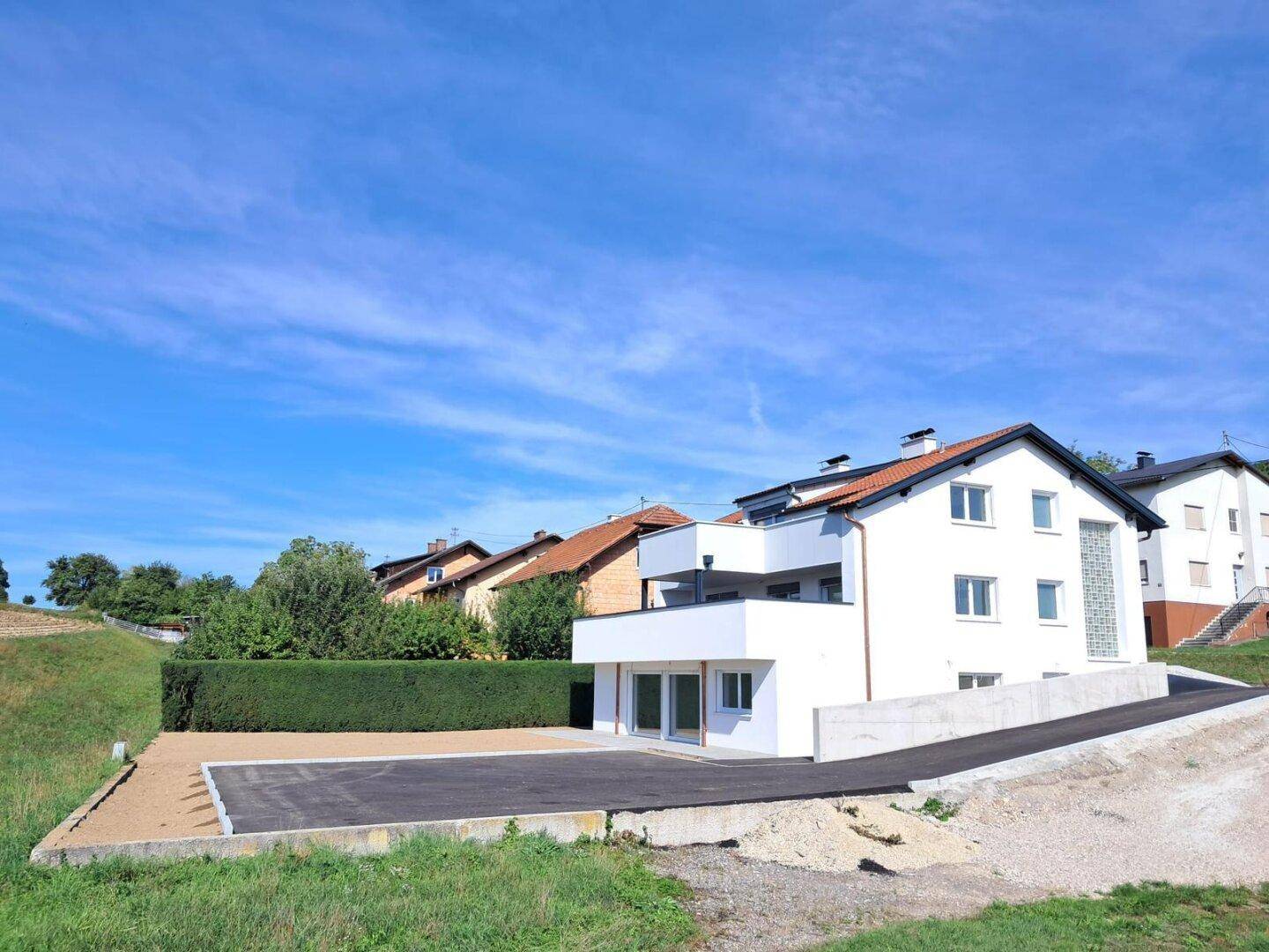 Modernes Einfamilienhaus mit weißer Fassade, großzügiger Auffahrt und ländlicher Umgebung unter blauem Himmel.