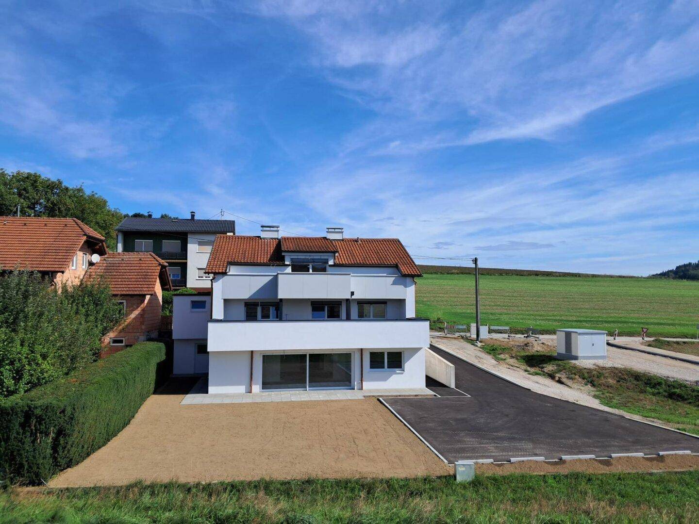 Neubau mit moderner Architektur, weißer Fassade und weitem Blick auf die umliegende Natur und Felder.