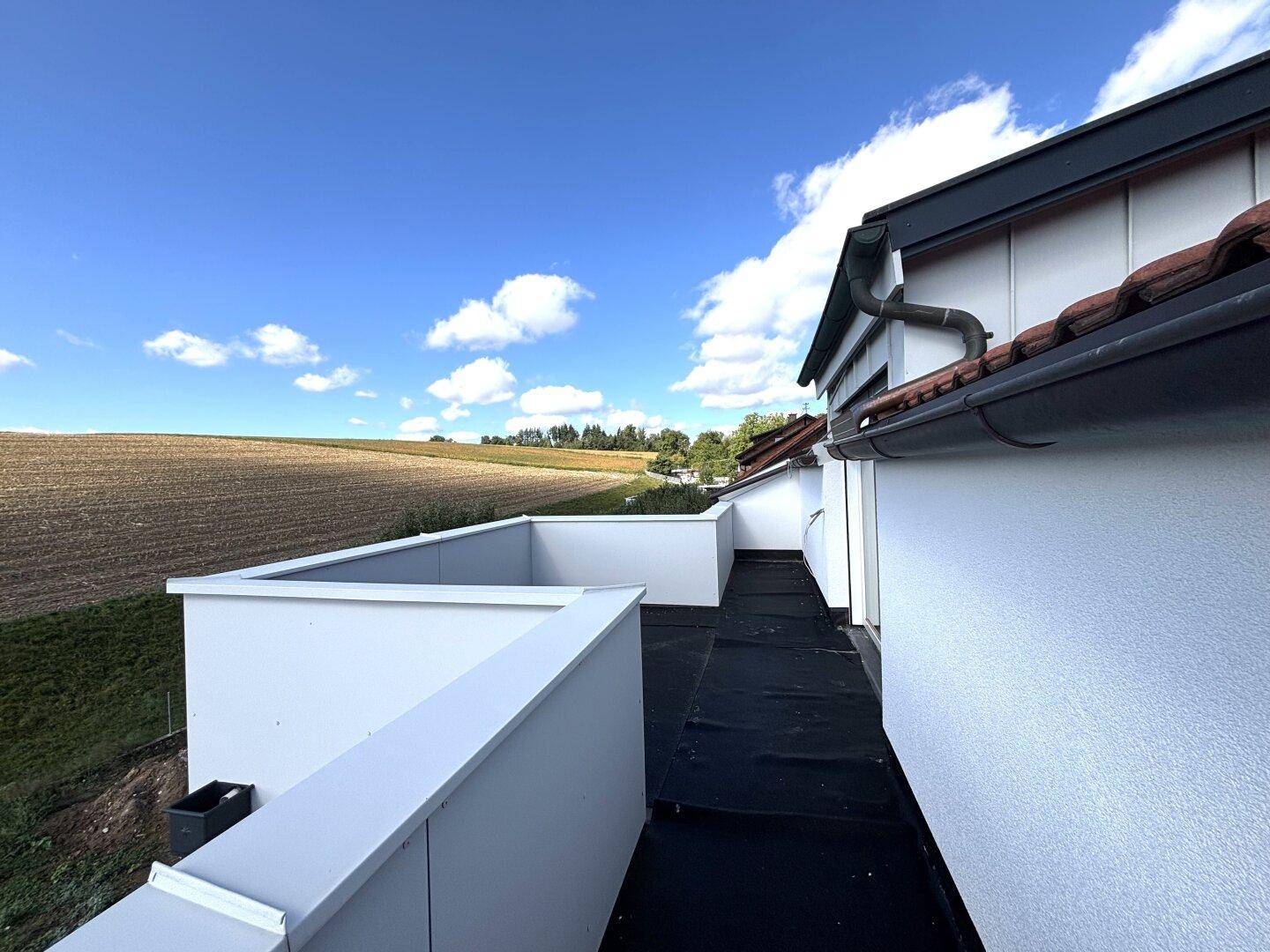 Unfertige Dachterrasse mit Blick auf die angrenzenden Felder und den blauen Himmel an einem sonnigen Tag.