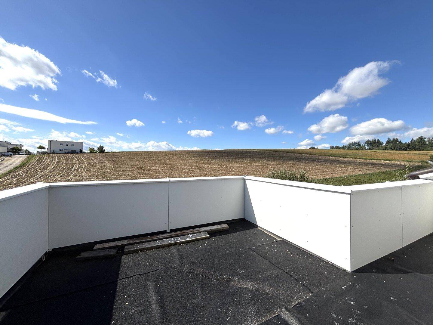 Geräumige Dachterrasse im Rohbau mit weitem Blick über die ländliche Umgebung und weite Felder.