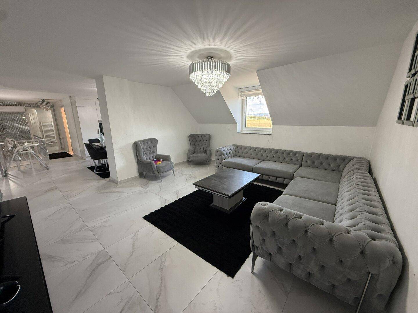 Geräumiges Wohnzimmer im Dachgeschoss mit großer Couch, eleganten Fliesen und Dachschräge.