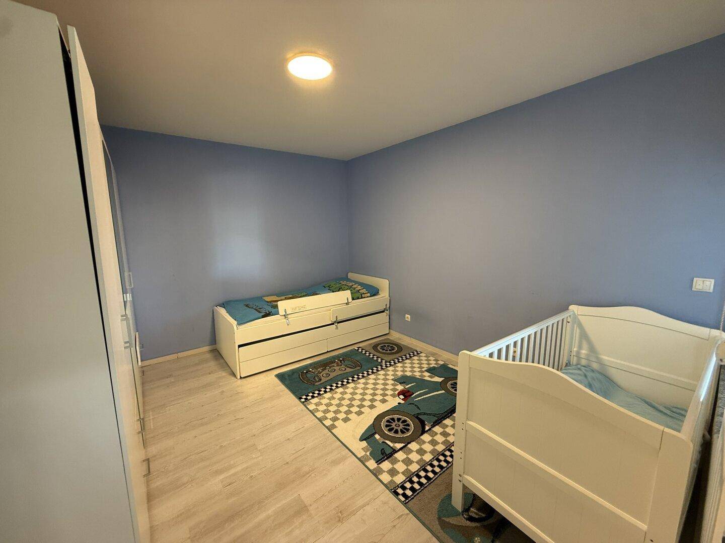 Kinderzimmer mit blauen Wänden, zwei Betten und hellem Laminatboden.