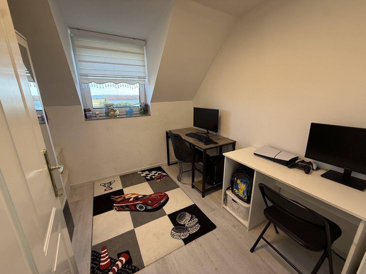 Kleines Arbeitszimmer im Dachgeschoss mit zwei Schreibtischen und Dachschräge.