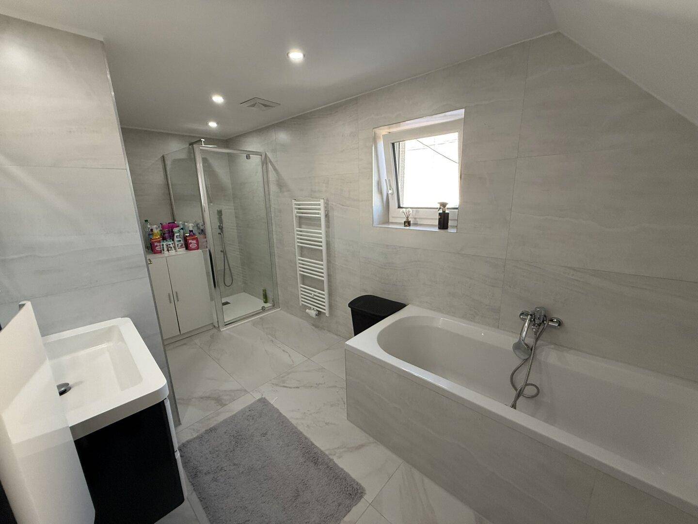 Modernes Badezimmer mit Badewanne, Duschkabine, Fenster und hellen Fliesen.