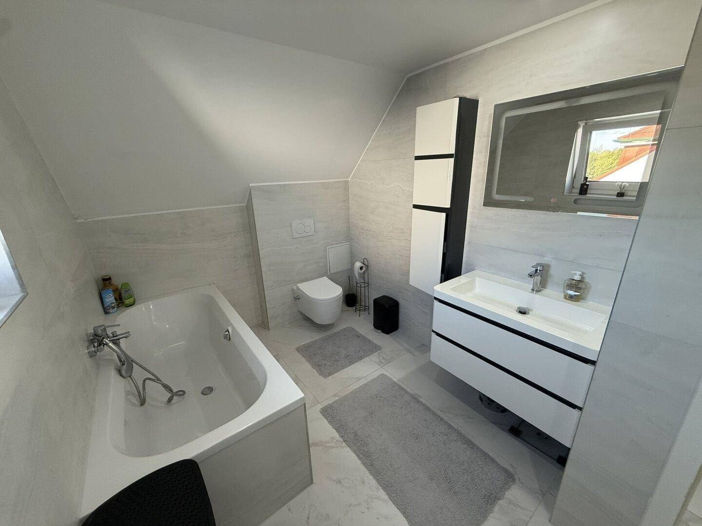 Helles Badezimmer mit Badewanne, modernem Waschtisch, Toilette und Fenster.
