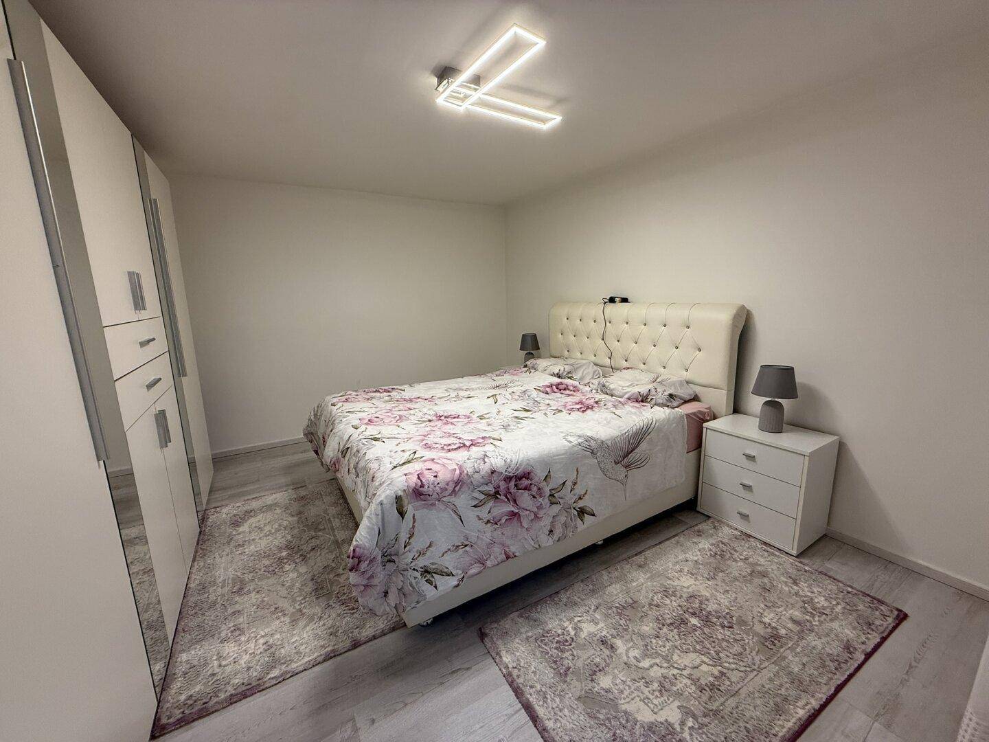 Helles Schlafzimmer mit modernem Bett, Nachttischen und großem Kleiderschrank.