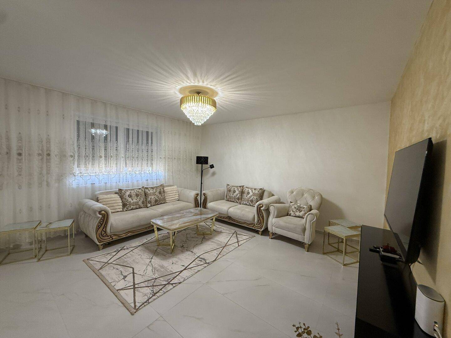 Elegantes Wohnzimmer mit beigen Sofas, Kronleuchter und gemustertem Teppich.