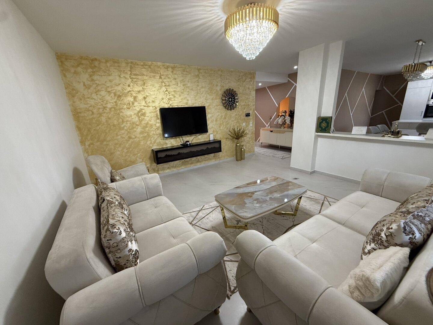 Stilvolles Wohnzimmer mit beigen Sofas, dekorativer Wand und modernem Couchtisch.