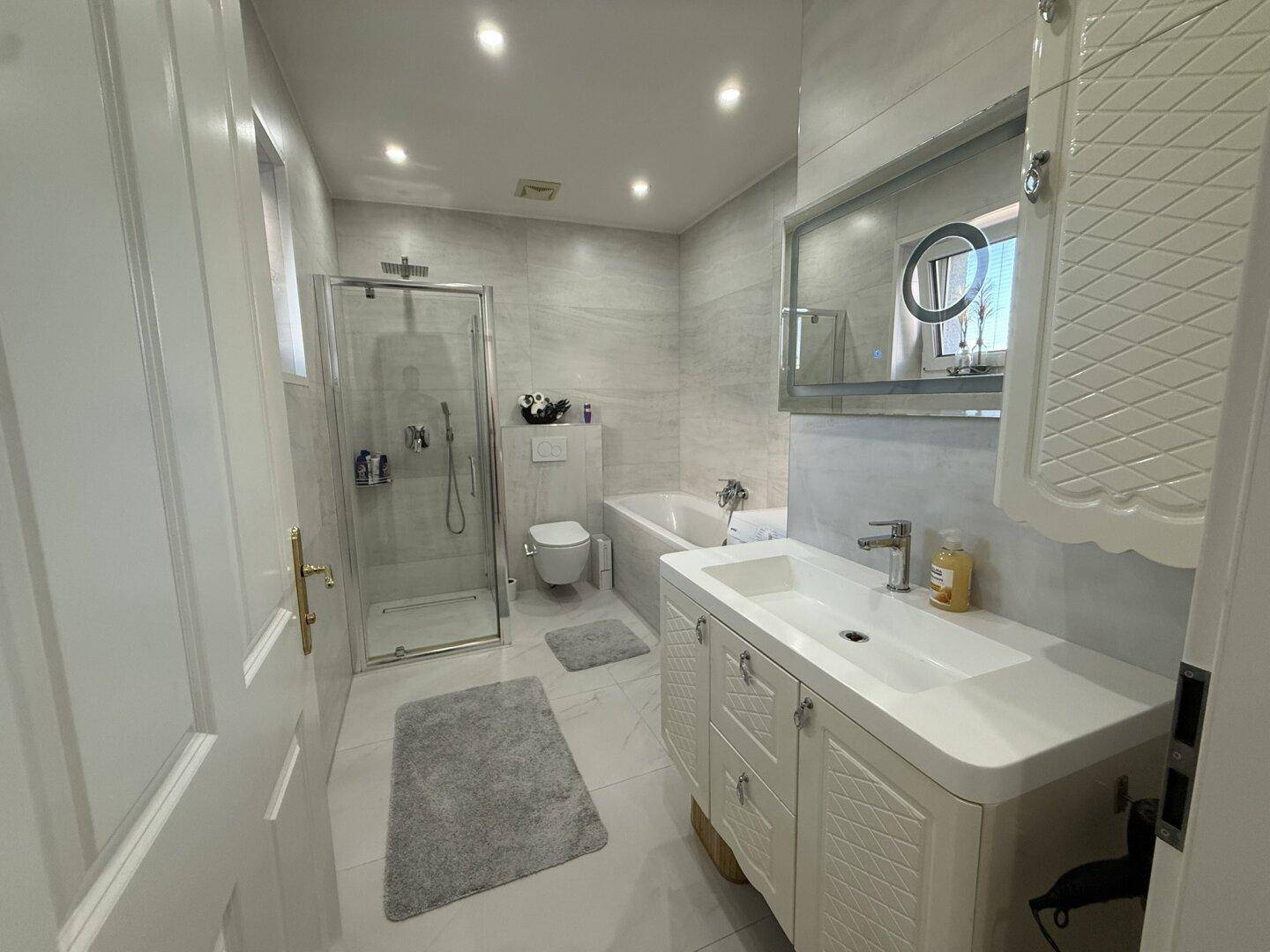 Modernes Badezimmer mit Dusche, Badewanne, Einzelwaschbecken und hellen Fliesen.