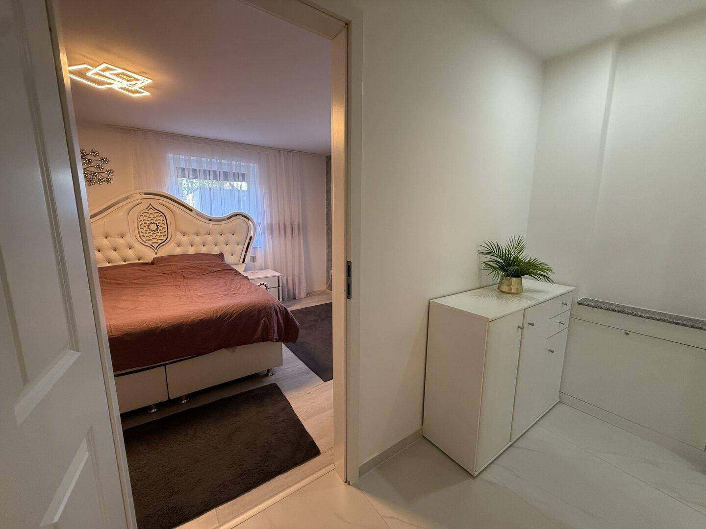 Blick vom Flur in ein helles Schlafzimmer mit großem Bett und Vorhängen.