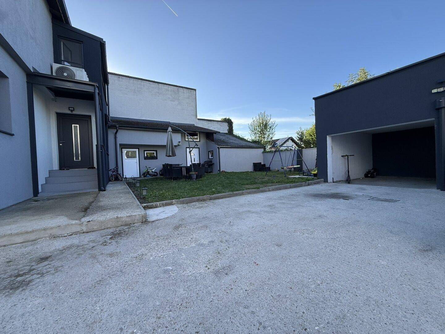 Außenansicht des Hauses mit Rasenfläche, gepflastertem Bereich und einer modernen Garage.
