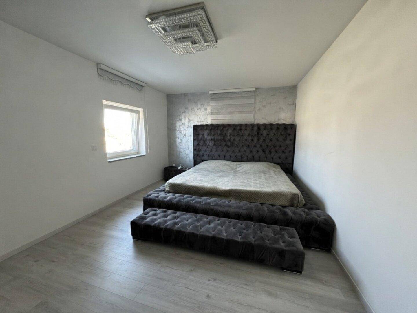Modernes Schlafzimmer mit großem gepolstertem Bett, Dachschräge und hellem Laminatboden.