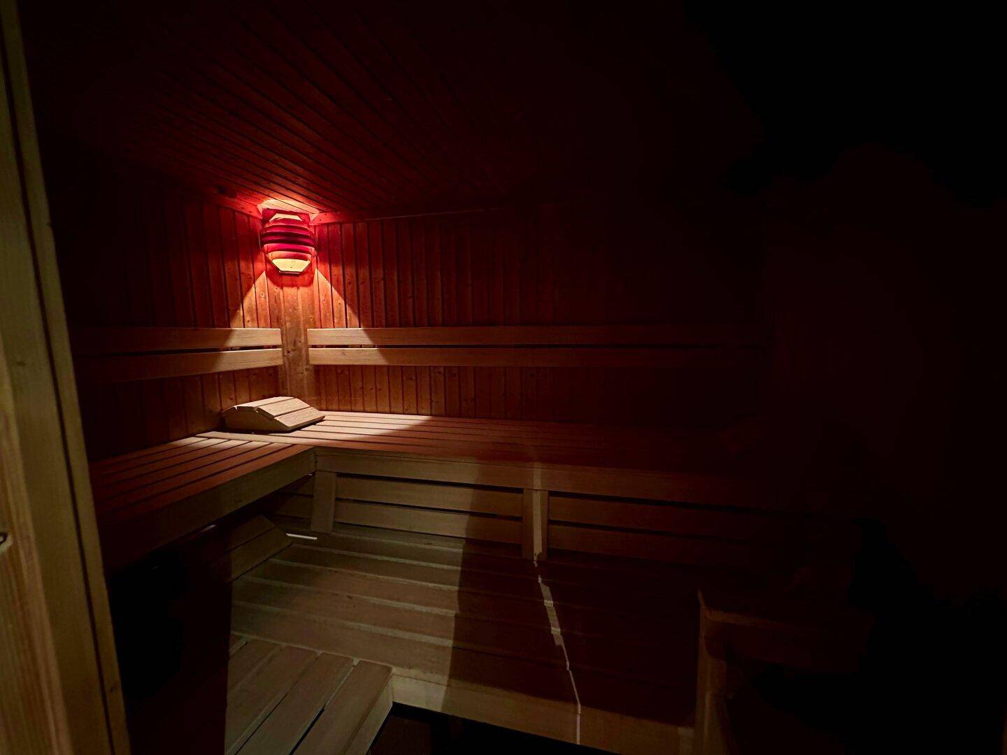 Innenansicht einer Holzsauna mit Bänken und gedämpfter Beleuchtung für Entspannung.