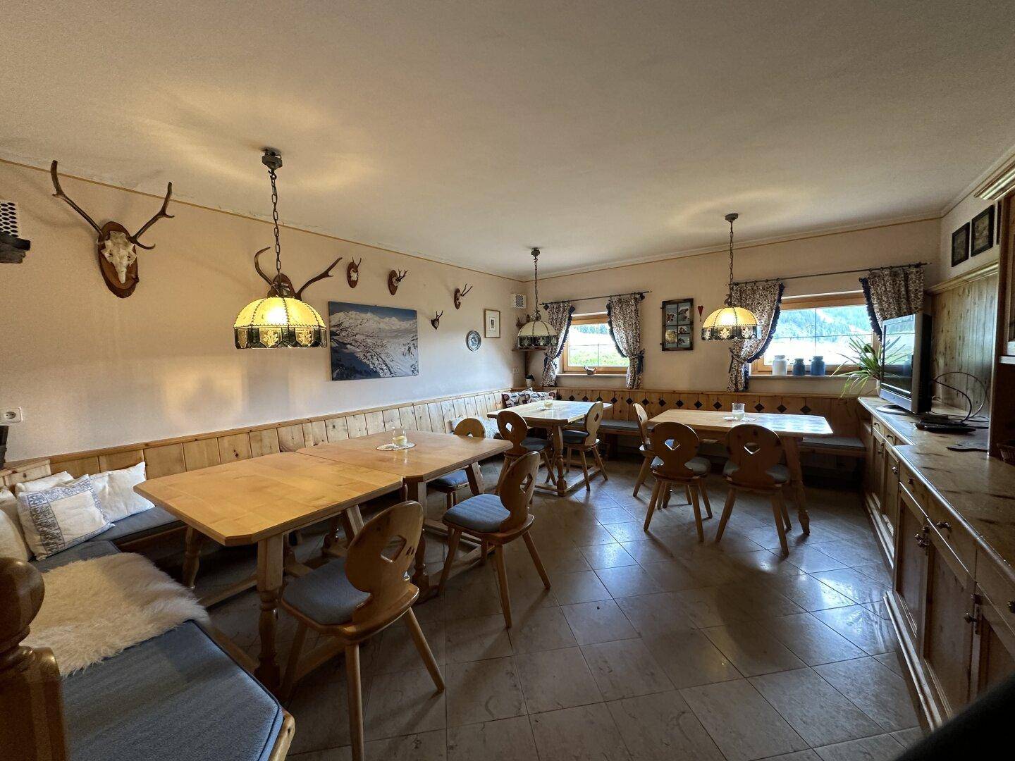 Großer traditioneller Speisesaal mit mehreren Tischen, Holzbänken und rustikaler Dekoration.