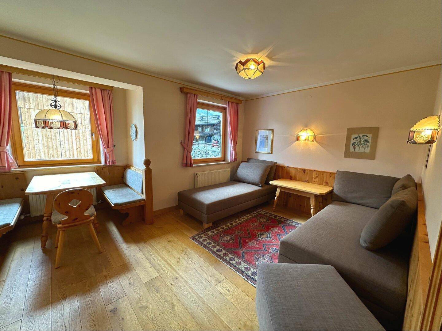 Gemütlicher Wohnbereich mit Sitzgelegenheiten, Holzboden und einem kleinen Essbereich am Fenster.