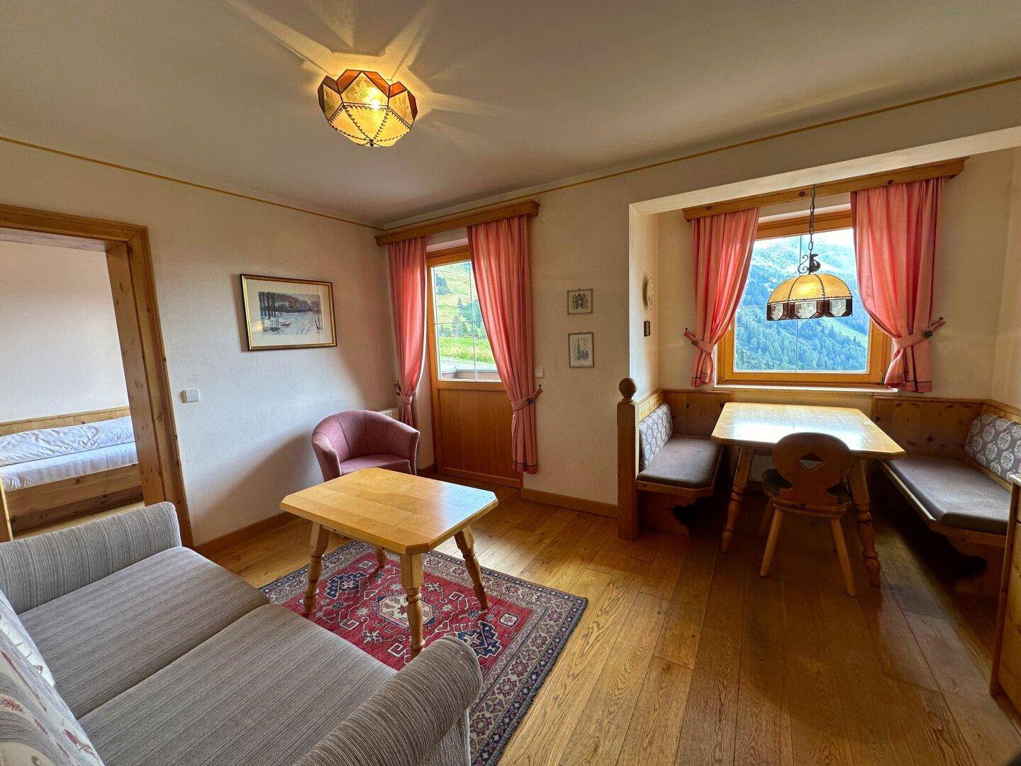 Wohn- und Essbereich mit Holzboden, traditionellen Möbeln und Bergblick durch die Fenster.