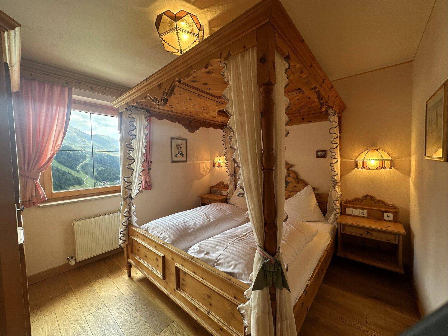 Gemütliches Schlafzimmer mit Himmelbett aus hellem Holz und Blick auf die Berglandschaft.
